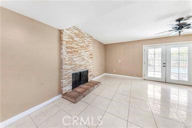 unfurnished living room featuring ceiling fan, light tile patterned flooring, a fireplace, baseboards, and french doors