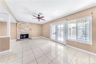 unfurnished living room with light tile patterned floors, ceiling fan, a fireplace, baseboards, and french doors