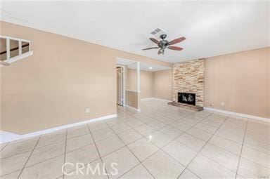 unfurnished living room featuring a fireplace, light tile patterned floors, visible vents, ceiling fan, and baseboards