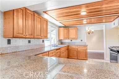 kitchen with light stone counters, stainless steel range, a sink, and backsplash