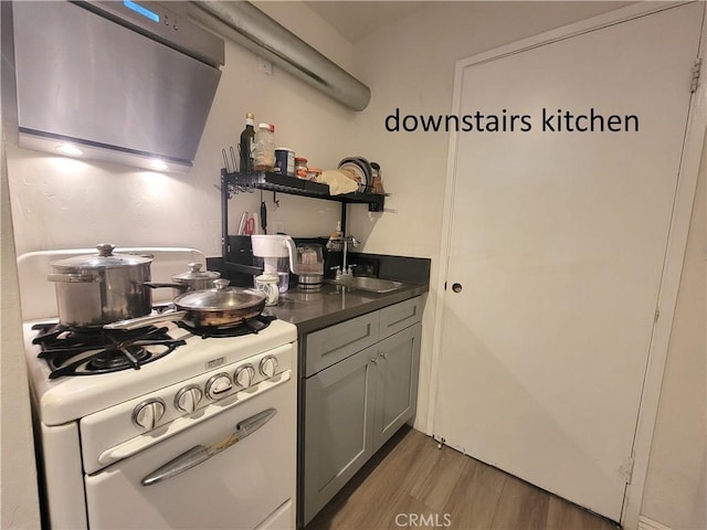 kitchen with dark countertops, white gas stove, light wood-type flooring, open shelves, and a sink