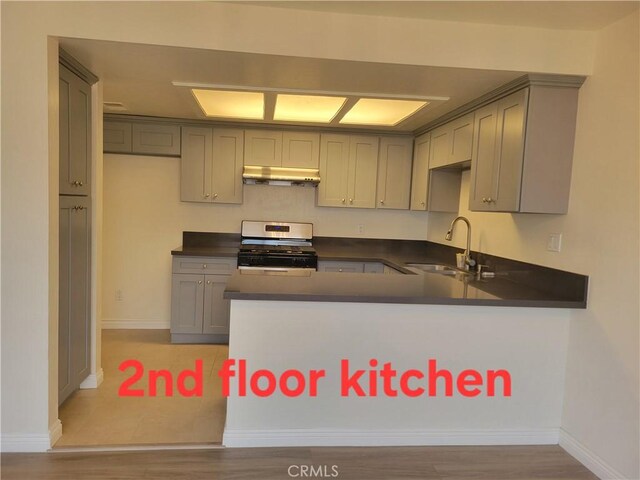 11865 Exline St Unit B, El Monte, CA 91732 - kitchen featuring gas range, under cabinet range hood, a sink, dark countertops, and a peninsula