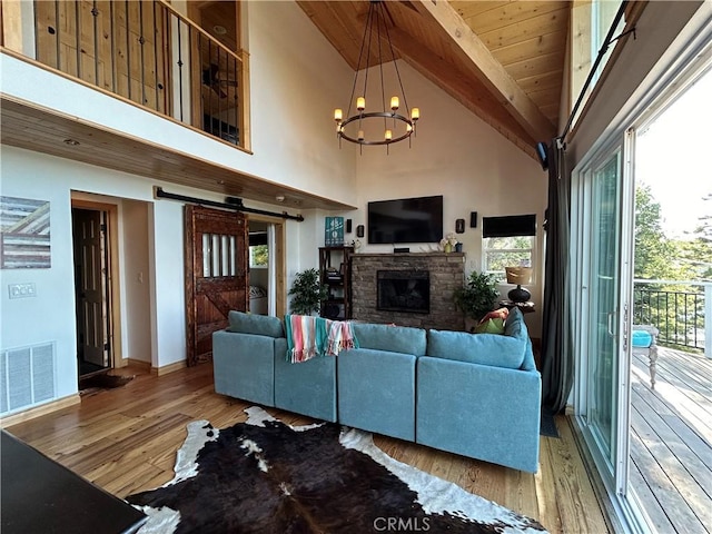 living area with visible vents, beamed ceiling, wood finished floors, a barn door, and a stone fireplace