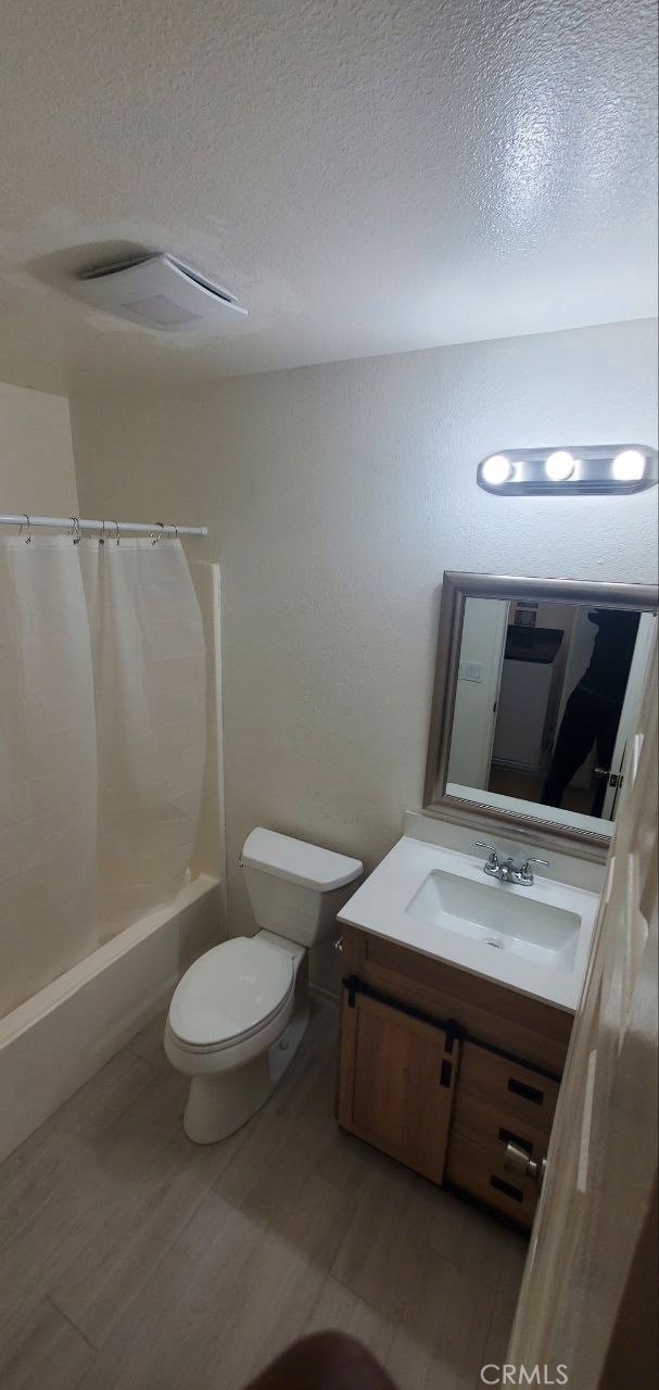 full bathroom featuring shower / bath combination with curtain, a textured ceiling, toilet, and vanity