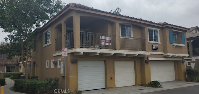 view of home's exterior featuring a balcony, central AC, stucco siding, concrete driveway, and a garage