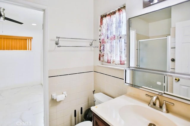 bathroom with tile walls, toilet, a ceiling fan, a stall shower, and vanity