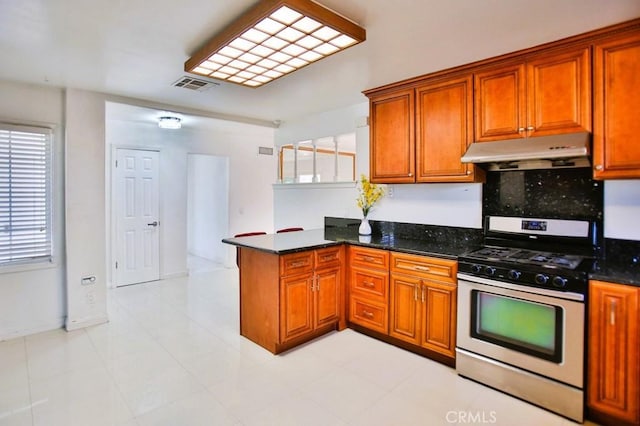 kitchen featuring under cabinet range hood, a peninsula, visible vents, stainless steel gas range, and brown cabinetry