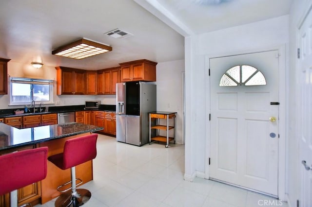 kitchen featuring dark countertops, visible vents, appliances with stainless steel finishes, brown cabinetry, and a sink