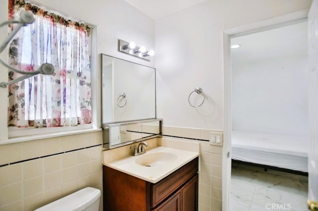 bathroom with ensuite bathroom, toilet, vanity, tile walls, and wainscoting