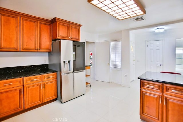 kitchen with dark stone countertops, stainless steel refrigerator with ice dispenser, visible vents, and brown cabinets