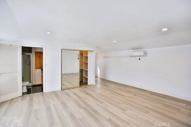 unfurnished bedroom with a wall unit AC, connected bathroom, recessed lighting, wood finished floors, and a closet