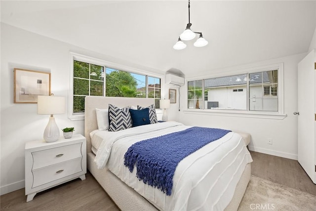 bedroom featuring baseboards, a wall unit AC, and wood finished floors