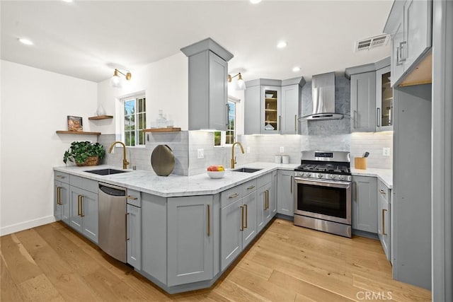 kitchen with visible vents, gray cabinetry, a sink, appliances with stainless steel finishes, and wall chimney range hood