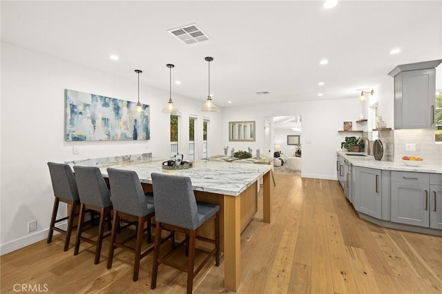 kitchen with light wood finished floors, visible vents, light stone counters, decorative backsplash, and gray cabinets