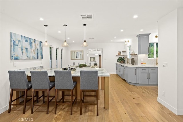 kitchen with light stone countertops, decorative backsplash, gray cabinets, a peninsula, and light wood-style flooring