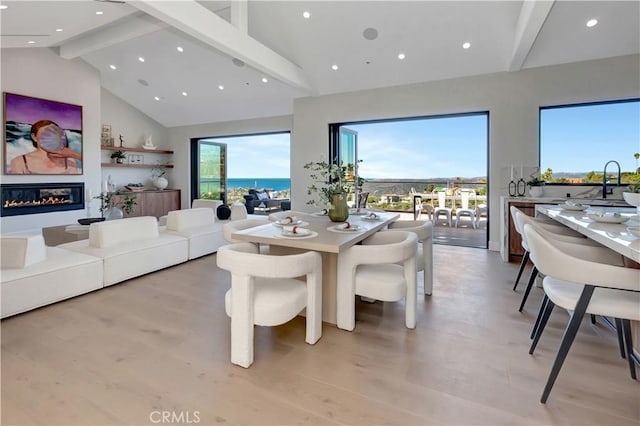 dining room featuring a glass covered fireplace, beam ceiling, a healthy amount of sunlight, and light wood-style flooring