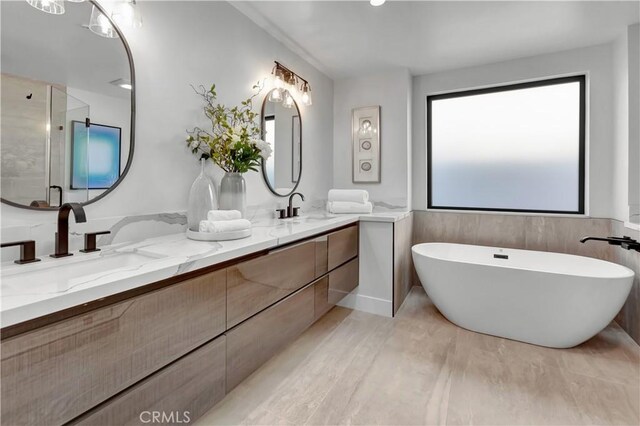 bathroom with a sink, a shower stall, a freestanding bath, and double vanity