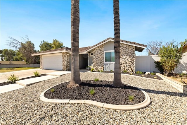 mid-century modern home with a garage, fence, stone siding, and driveway