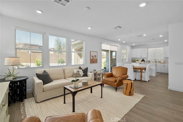 living room featuring light wood-style floors, baseboards, visible vents, and recessed lighting