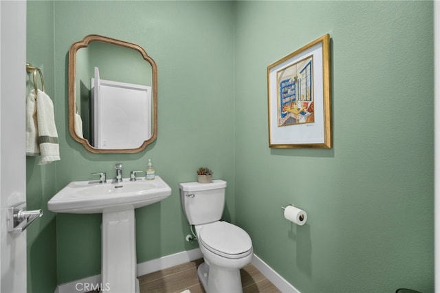 bathroom featuring toilet, a sink, baseboards, and wood finished floors