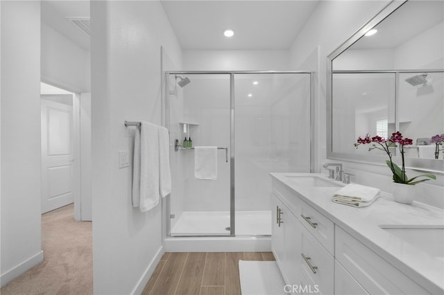 bathroom with double vanity, wood finished floors, a stall shower, and a sink