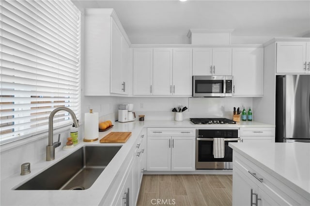 kitchen featuring a sink, light wood-style floors, white cabinets, light countertops, and appliances with stainless steel finishes