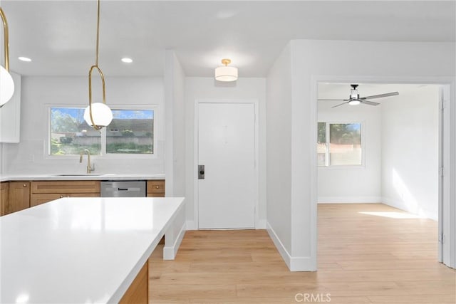 kitchen with a sink, light wood-type flooring, light countertops, and stainless steel dishwasher