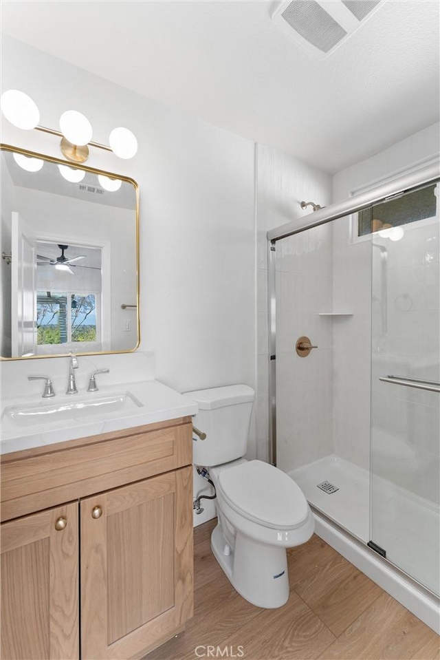 full bath featuring toilet, a ceiling fan, a shower stall, vanity, and wood finished floors