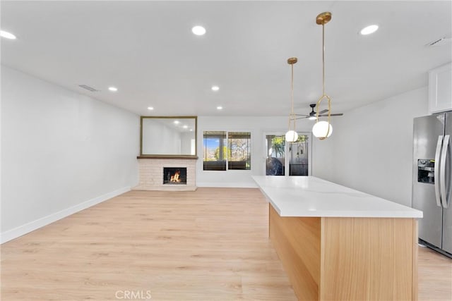 kitchen with stainless steel refrigerator with ice dispenser, recessed lighting, light countertops, light wood-style floors, and a brick fireplace