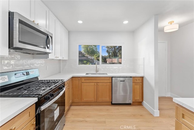 kitchen with light wood finished floors, appliances with stainless steel finishes, a sink, light countertops, and backsplash