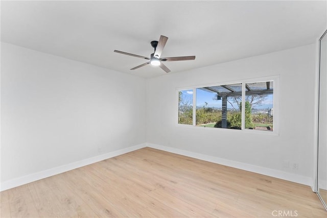 spare room featuring a ceiling fan, light wood-style flooring, and baseboards