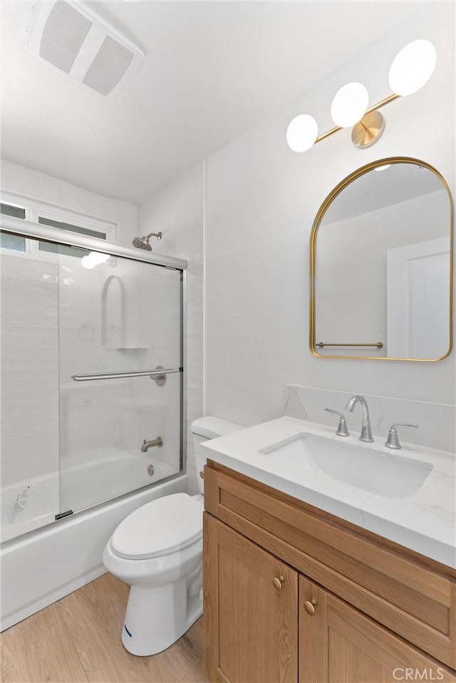 bathroom featuring visible vents, toilet, enclosed tub / shower combo, wood finished floors, and vanity