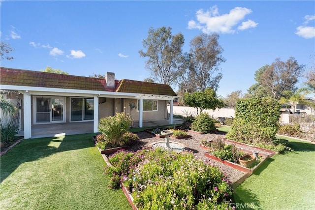 back of property with a chimney, stucco siding, a lawn, a patio area, and a garden