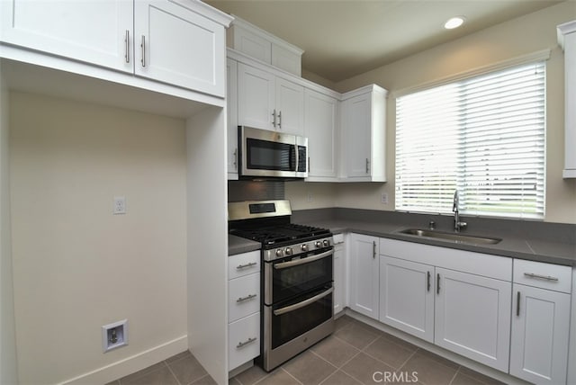 kitchen featuring stainless steel appliances, dark tile patterned flooring, a sink, white cabinets, and dark countertops