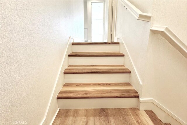 stairway featuring baseboards, wood finished floors, and a textured wall