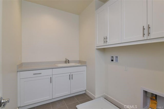 laundry area featuring dark tile patterned floors, washer hookup, a sink, baseboards, and cabinet space