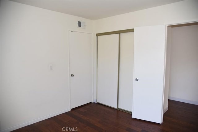 unfurnished bedroom with visible vents, baseboards, a closet, and dark wood-style flooring