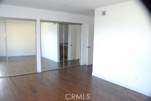 unfurnished bedroom featuring visible vents, two closets, and wood finished floors