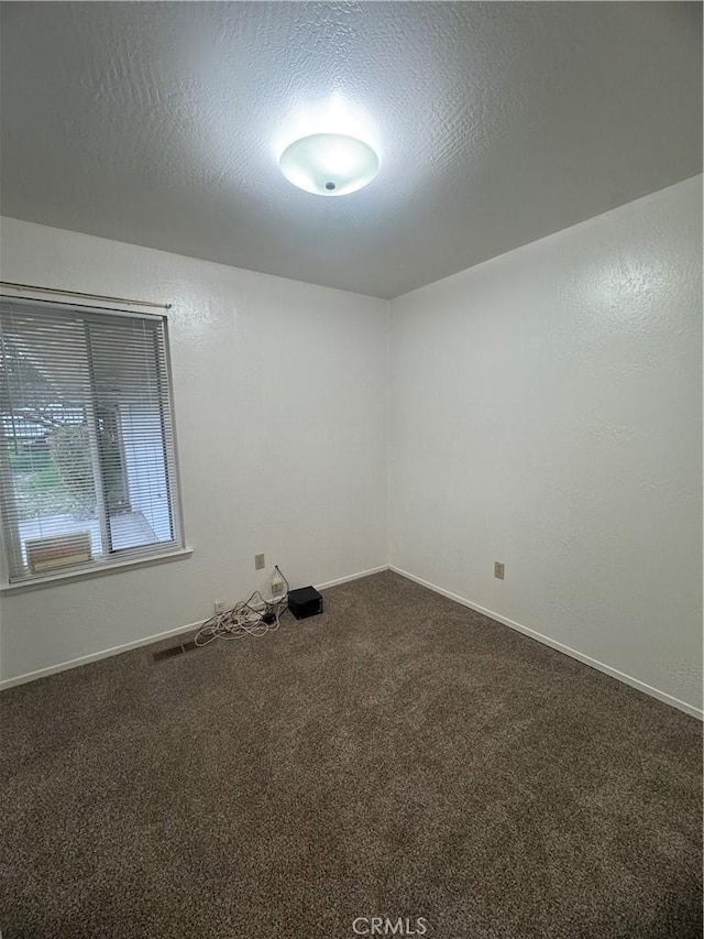 empty room featuring dark carpet, a textured ceiling, and baseboards