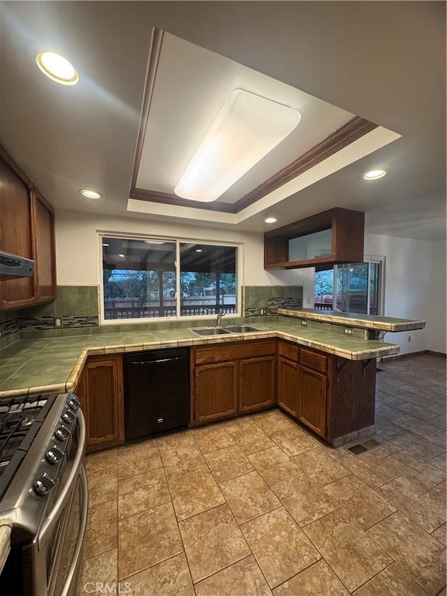 kitchen featuring black dishwasher, a sink, a raised ceiling, and tile counters