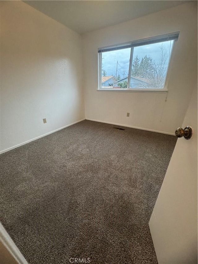 empty room featuring dark colored carpet, visible vents, and baseboards