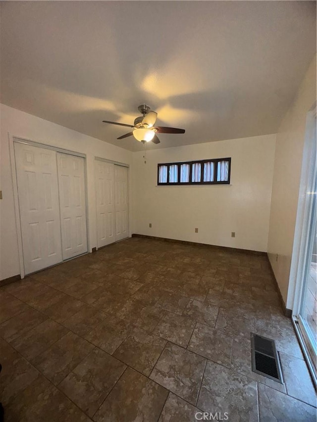 unfurnished bedroom featuring baseboards, ceiling fan, visible vents, and multiple closets