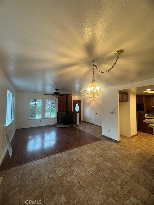 unfurnished living room with a textured ceiling, ceiling fan, wood finished floors, baseboards, and a wood stove