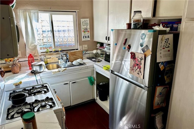 kitchen featuring tile counters, white range with gas stovetop, freestanding refrigerator, and white cabinets