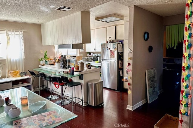 kitchen with a peninsula, visible vents, white cabinetry, freestanding refrigerator, and dark wood-style floors