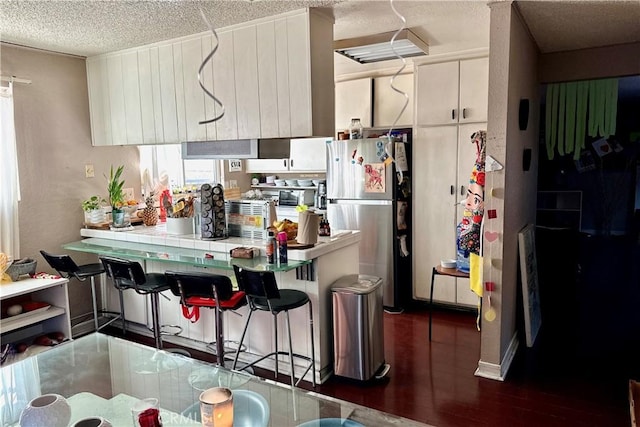 kitchen with white cabinets, a breakfast bar area, freestanding refrigerator, a peninsula, and a textured ceiling