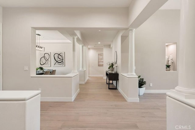 hall featuring light wood finished floors, baseboards, and ornate columns