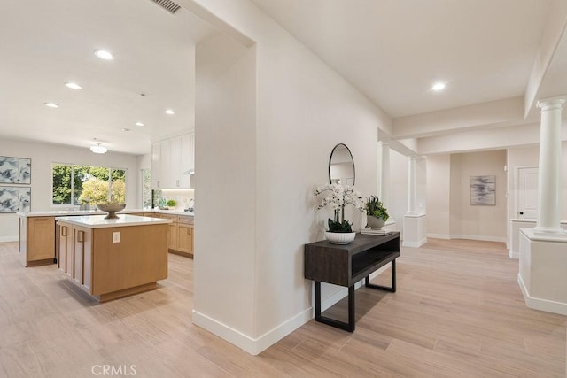 hallway featuring decorative columns, light wood-style floors, and baseboards