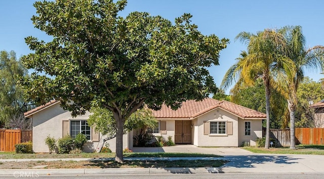 mediterranean / spanish house with stucco siding, a tile roof, and fence