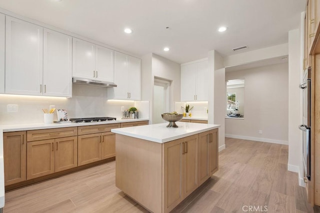 kitchen featuring visible vents, a kitchen island, under cabinet range hood, light countertops, and black gas stovetop